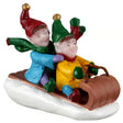 This image shows what this Lemax Santa's Wonderland figurine looks like on a white background. It was designed to look like two elves riding a brown toboggan downhill. The elf in front is wearing a yellow shirt, a green hat with a gold bell, green gloves, a red/green scarf, blue pants and brown shoes. The elf in back is wearing a blue jacket, a red hat with a gold bell, purple gloves, a green scarf, purple pants and green shoes.