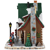This image shows what the side of this building looks like. It has a tall stone chimney that's decorated with a large wreath. There's a shovel leaning up against the chimney, as well as a pile of firewood.