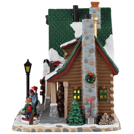 This image shows what the side of this building looks like. It has a tall stone chimney that's decorated with a large wreath. There's a shovel leaning up against the chimney, as well as a pile of firewood.