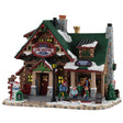 This image shows what this Lemax building looks like on a white background. It was designed to look like a large log cabin turned into a ski school. There's snow on the roof and on the stone sidewalk. There's a snowman on the corner. People are at the counter registering and there are people getting ready to start skiing.
