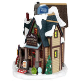 This image shows one of the sides of the building. There are signs on the building that read "Quality Mountain Gear" and "Snowcap Cafe Coffee & Eats." The roof and ground are covered in snow. Near the front door, there are some tubes for sledding.