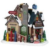 This image shows what this Lemax building looks like on a white background. It looks like it was a large log cabin with a stone chimney that has been turned into a bunch of different shops. Outside around the porch, there are skis, sleds and snowboards leaning, waiting for people to come out and use them. There are signs that read "Winter Sports Supplies," "Custom Products," "Bighorn Peak Mountain Sports Snow Gear," "Special! Free goggles when you buy our ski package" and "Fresh apple and cherry pies!"