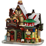This image shows what this Lemax Vail Village lighted building looks like on a white background. It was designed to look like a cottage turned into a restaurant. On the roof, there's a large, fake fondue pot. There's a fondue station booth on the sidewalk.