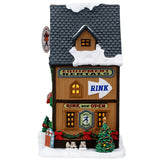 This image shows what the side of this building looks like. The roof and the sidewalk both have snow on them. There are a few pairs of skates leaned up against the wall. There's also a decorated Christmas tree and a green garland with red bows.