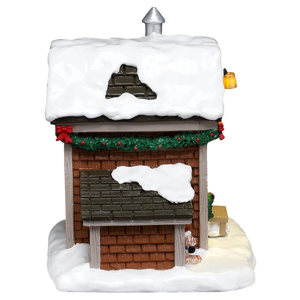 This is image shows what the side of the house looks like. You can see the green garland with red bows along the roof and the small dog house on the ground.