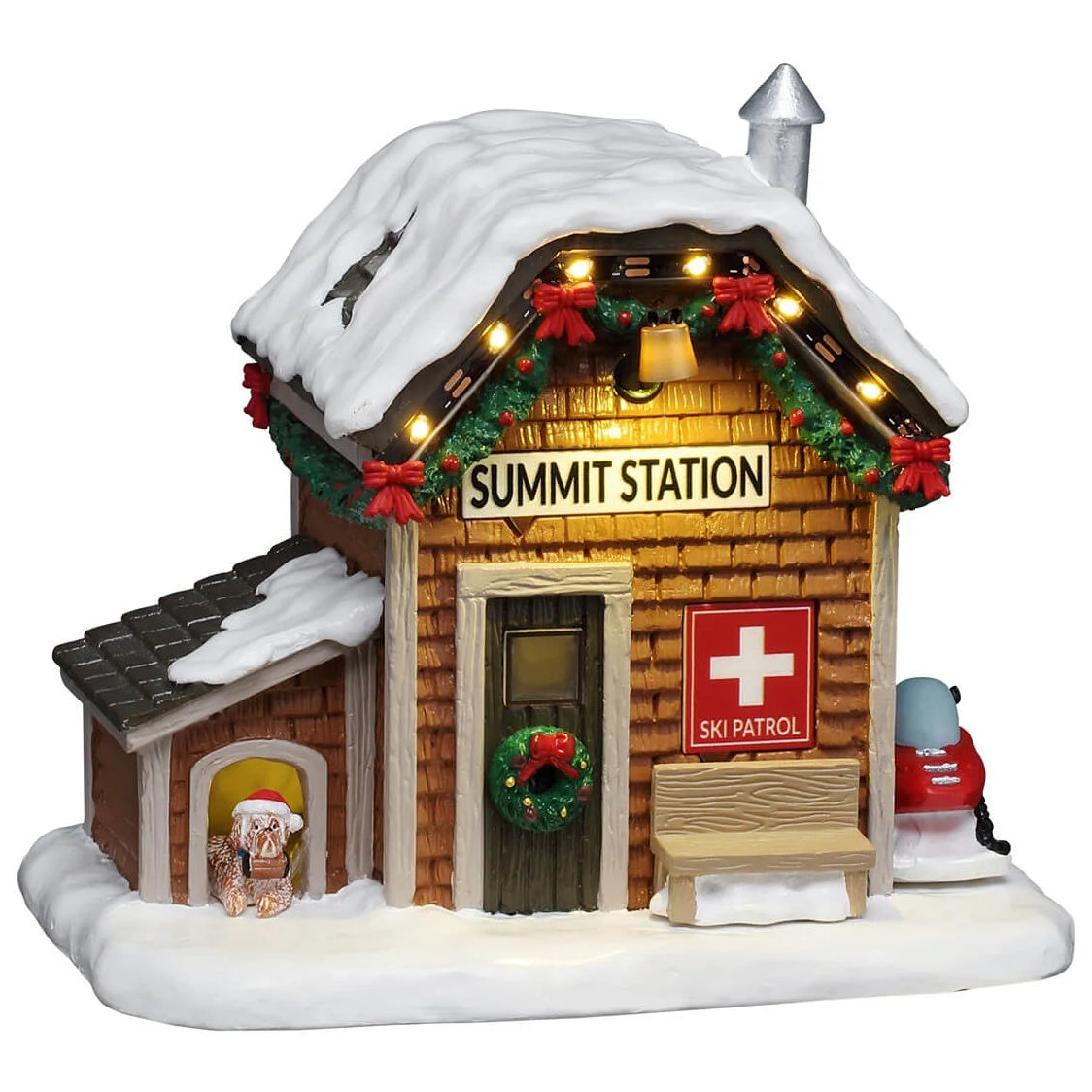 This image shows what this Lemax table accent looks like on a white background. It was designed to look like a small ski patrol station. The roof and the ground is covered in snow. There's a small dog house on the left side and a red snowmobile on the right side. There's a dog in the dog house wearing a Santa hat. There's a wreath on the front door and a garland decorated with red bows along the roofline. There's a bench next to the front door and a sign that reads "SKI PATROL."