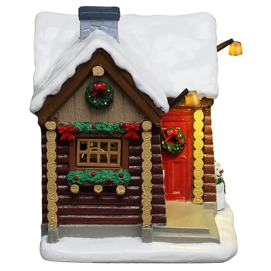 This is another angle of the log cabin. There's a decorated wreath hanging on the red front door, as well as a wreath hanging near the stone chimney.