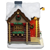 This is another angle of the log cabin. There's a decorated wreath hanging on the red front door, as well as a wreath hanging near the stone chimney.