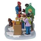 This image shows what this piece looks like from the side. You can see someone getting ready to flip the food on the grill and there are people pouring drinks into cups. One of the dogs has a cheeseburger in its mouth.
