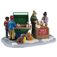 This image shows what this Lemax piece looks like on a white background. It was designed to look like four people grilling together in the snow. There are also two dogs begging for food. There's a sign that reads "Ted's Hot Toddies 21+ Only."
