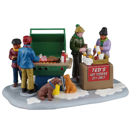 This image shows what this Lemax piece looks like on a white background. It was designed to look like four people grilling together in the snow. There are also two dogs begging for food. There's a sign that reads "Ted's Hot Toddies 21+ Only."