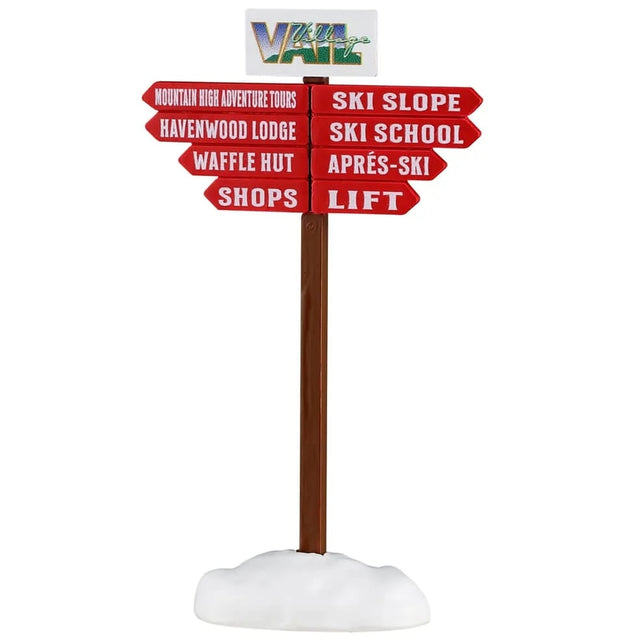 This image shows what this Lemax Village accessory looks like on a white background. It was designed to look like a sign pointing in different directions to help you know where to go. The sign reads "Vail Village" and the red arrows point toward the Mountain High Adventure Tours, the Havenwood Lodge, the Waffle Hut, Shops, Ski Slope, Ski School, Apres-Ski, Lift."