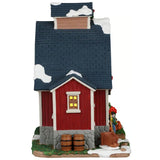 This image shows what the other side of this building looks like. There's some snow on the roof and on the grass. There's also a wheelbarrow and a few wooden kegs.