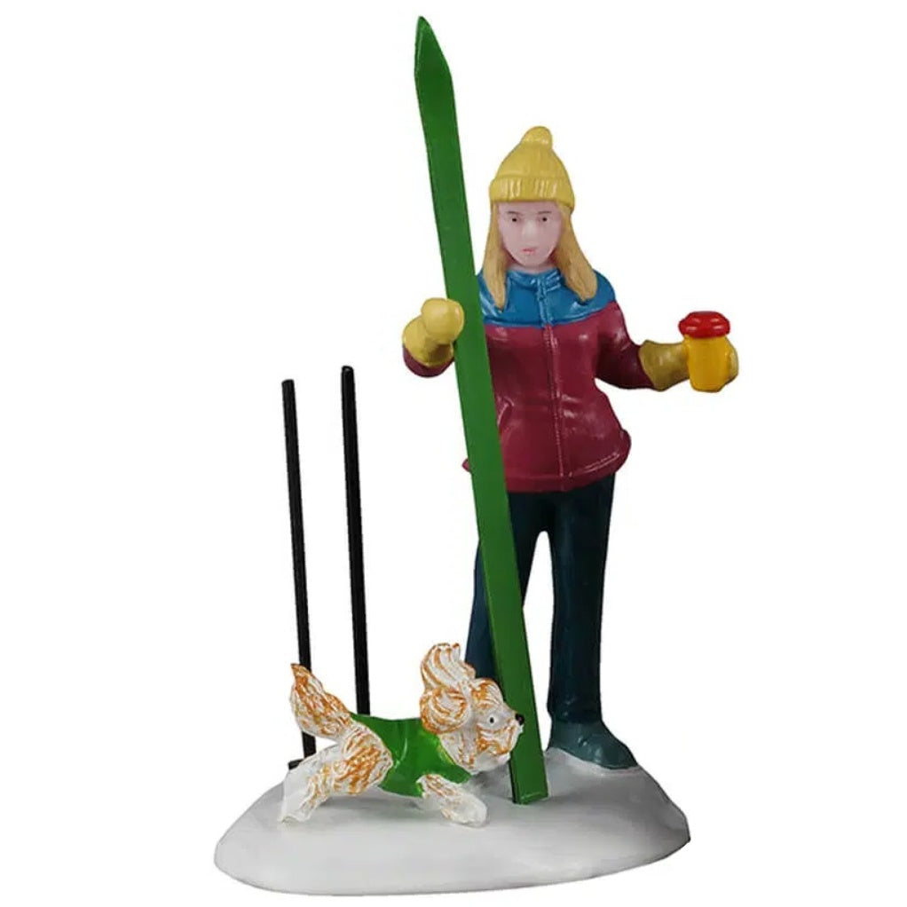 This image shows the mom figurine standing in a pile of snow. She's wearing a yellow hat, a blue/maroon coat, blue pants, blue boots and yellow gloves. She's holding a red and yellow colored coffee cup and her green ski. Her black ski poles are standing upright in the snow. The dog is running in the snow. He's white and orange and wearing a green sweater.