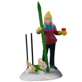 This image shows the mom figurine standing in a pile of snow. She's wearing a yellow hat, a blue/maroon coat, blue pants, blue boots and yellow gloves. She's holding a red and yellow colored coffee cup and her green ski. Her black ski poles are standing upright in the snow. The dog is running in the snow. He's white and orange and wearing a green sweater.