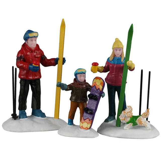 This image shows what these three Lemax Vail Village figurines look like on a white background. They were designed to look like a family about to enjoy time in the snow. The mom and dad have skis and the young boy has a snowboard. There's also a dog wearing a green sweater running around.