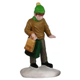This image shows what the little boy figurine looks like on a white background. He's wearing a green hat, a green scarf, a brown sweater, khaki pants and black boots. He's holding a gold bag and a dark green bag.
