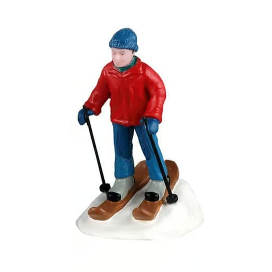This image shows one of the figurines. It was designed to look like a man skiing downhill. He's wearing a blue knit hat, a red jacket, a blue scarf, blue pants, blue gloves, brown skis and black ski poles.