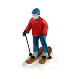 This image shows one of the figurines. It was designed to look like a man skiing downhill. He's wearing a blue knit hat, a red jacket, a blue scarf, blue pants, blue gloves, brown skis and black ski poles.