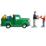 This image shows what these figures look like from the side. The truck is green and full of toys. The pastor is wearing a blue sweater, khaki pants and brown shoes. He's holding a cardboard box of toys. The little girl is taking a teddy bear out of the box.