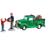 This image shows what these Lemax figures look like on a white background. The scene is designed to look like a pastor donating toys from the back of his green truck. He's handing a box of toys to a young girl.