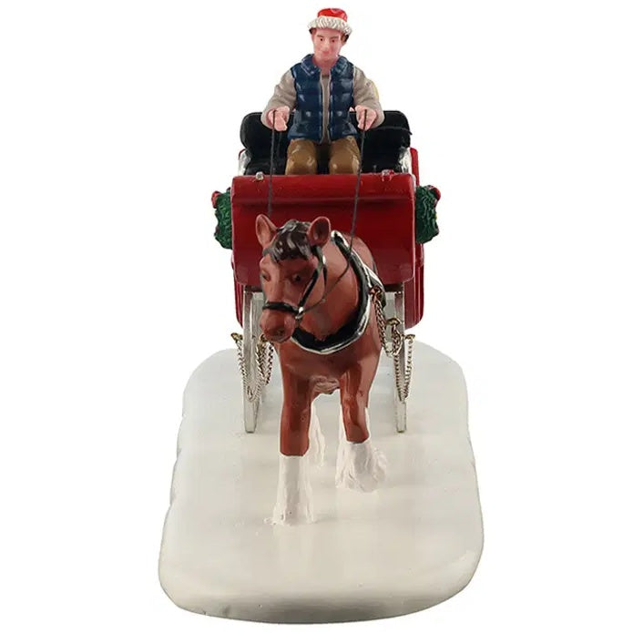 This image shows what the table accent looks like from the front. The driver of the sleigh is wearing a Santa hat, a grey hoodie with a blue puffer vest, brown pants and black shoes.