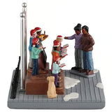 This image shows this table piece from the side. You can see that the choir has people playing instruments in the back row and there are people holding red song books in the front row. There are two teachers standing in front of them, directing them.