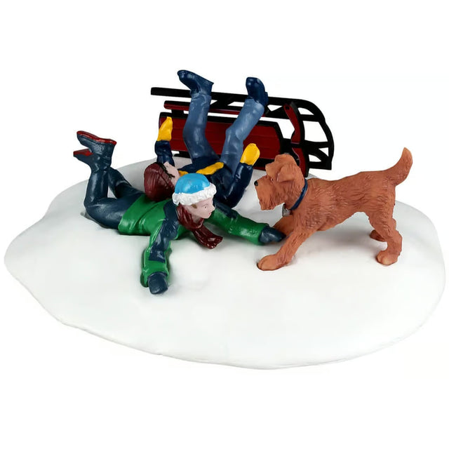 This image shows what this Lemax table accent looks like on a white background. It was designed to look like two boys have crashed their sled in the snow and a dog came up to see if they were okay. The sled is a maroon color.
