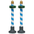 This image shows what these two Lemax Village accessories look like on a white background. These were designed to look like decorative poles. They're blue and white striped with a gold bauble on top. Near the top of the pole, there's a green garland wrapped around it.