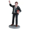 This image shows what this Lemax General Collectibles figurine looks like on a white background. It was designed to look like a young man with brown hair, wearing a black suit with a dark blue tie. He's waving with one hand and holding a Bible with the other.