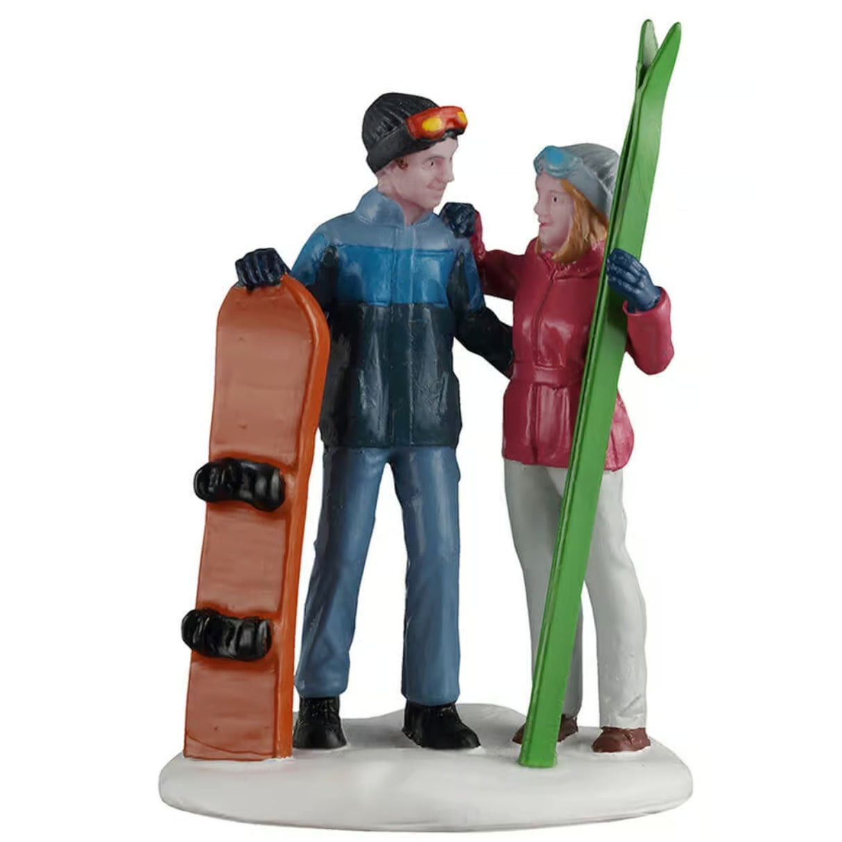 This image shows what this Lemax General Collectibles figurine looks like on a white background. It was designed to look like a man and a woman embracing in the snow. The man is wearing a black knit hat with goggles on, along with a blue jacket, blue jeans and black shoes. He's holding an orange snowboard. The woman is wearing a gray knit hat with goggles on, along with a red jacket, tan pants and brown shoes. She's holding a pair of green skis.