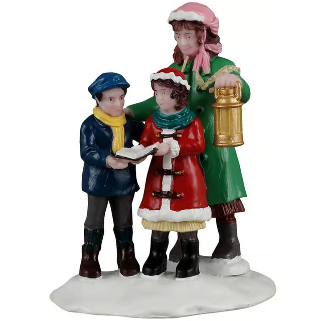 This image shows what this Lemax Caddington Village figurine looks like on a white background. It was designed to look like a mom and two kids singing carols. Mom is wearing a pink bonnet, a green jacket, a brown dress and black boots. The little boy is wearing a blue hat, a yellow scarf, a blue jacket, grey pants and black boots. The little girl is wearing a red hat, a green scarf, a red/white coat, a yellow dress and black boots. The mom is holding a gold lantern and the kids are holding the songbook.