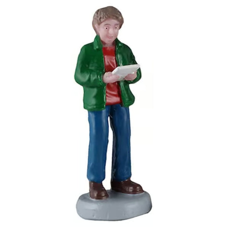 This image shows a young boy figurine holding a sheet of music and singing. He has light brown hair and is wearing a green jacket, a red shirt, blue jeans and brown shoes.