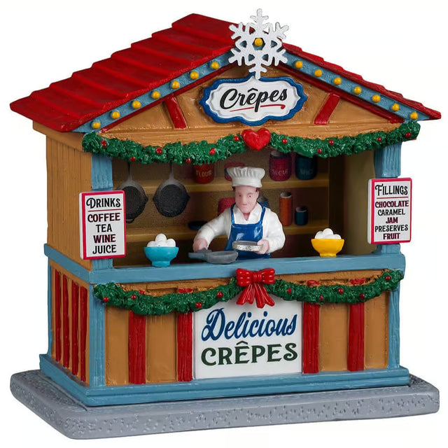 This image shows what this Lemax table accent looks like on a white background. It was designed to look like a wooden booth that sells crepes. The roof is red with a blue and yellow trim. There's also a white snowflake on the roof. Underneath the counter, the booth is decorated with green garland and red bows. There's a person behind the counter about to crack an egg. There are signs that read "Drinks: Coffee, Tea, Wine, Juice" and "Fillings: Chocolate, Caramel, Jam, Preserves, Fruit."
