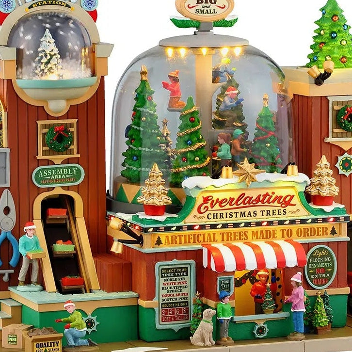 This is an up close view of the Everlasting Christmas Tree shop. The sign above the front booth reads "Artificial Trees Made to Order." A man is working in the assembly area while another man is closing up boxes of tree stands.