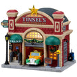This image shows what this Lemax building looks like on a white background. It was designed to look like a red barn turned into a garage for taxis. There's a large, gold star on the roof. There are decorative garlands and wreaths. Inside the garage, there's a yellow and green colored taxi.