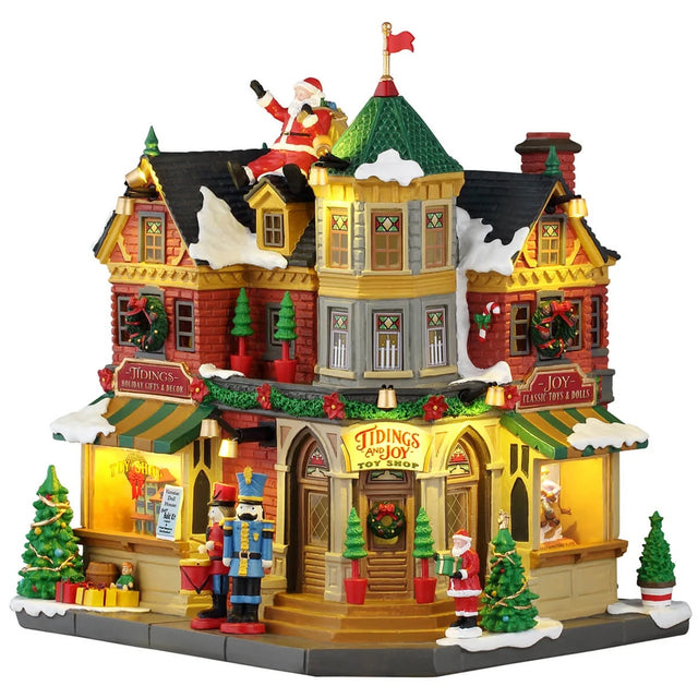 This image shows what this Lemax building looks like on a white background. It was designed to look like a very large toy shop. There's a large fake Santa sitting on the roof, waving. The roof and sidewalk are covered in snow. There are Christmas decorations all over, as well as some nutcrackers standing guard by the front door.