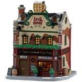 This image shows what this Lemax building looks like on a white background. It was designed to look like a tall cottage turned into a pub. There's a large, fake gold mug of beer on the roof. There's a window near the front door and you can see people drinking inside. There are kegs of beer and potted trees on the sidewalk, along with snow.