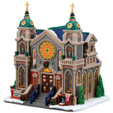 This image shows what this Lemax building looks like on a white background. It was designed to look like a very large, intricate cathedral. There are gold steeples, gold crosses and stained glass windows. There's a nativity scene near the front door.