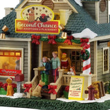 This is an up close view of the lighted building. You can see there's a dog wearing a Santa hat near the mailbox and there's a dog on a red leash standing on the front stairs. The sign near the fire hydrant reads "Volunteer Coordinators Needed! Pet Adoption & Foster Placement."