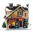 This image shows what this Lemax building looks like on a white background. It was designed to look like a house turned into a pie shop. The snow and the sidewalk are covered in snow. There's a walk-up counter with a person behind the counter serving pies. There's a table near the front door, along with a snowman holding a pie.