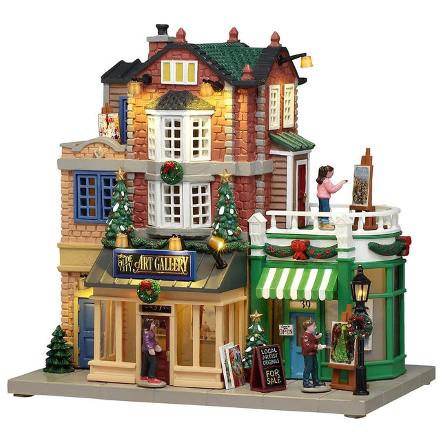 This image shows what this Lemax building looks like on a white background. It was designed to look like a tall art gallery. There's a balcony on the second floor where there's a woman painting. There are people on the sidewalk looking at the art that's on display outside. There are decorated Christmas trees and wreaths all over. 