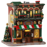 This image shows what this Lemax building looks like on a white background. It was designed to look like a tall building turned into a pizzeria. There's a balcony on the second floor that has a bunch of flower planters and a bike. There's a red, green and white awning over the front door. There are signs and a decorated Christmas tree on the sidewalk.