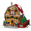 This image shows what this Lemax building looks like on a white background. It was designed to look like a yellow barn that sells live trees. The roof and the sidewalk are covered in snow. There are garlands, wreaths and red bows everywhere. There are people standing near the front door. Off to the right, there's a red fenced in area with a bunch of trees.