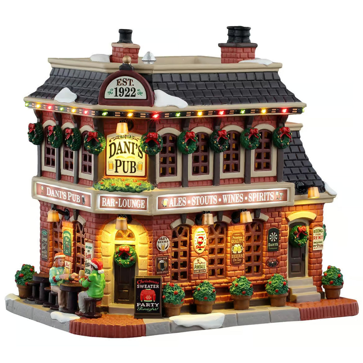 This image shows what this Lemax Caddington Village lighted building looks like on a white background. It was designed to look like a large, old-timey cottage turned into a pub. The windows are decorated with wreaths and the sidewalk is decorated with potted plants. There are two people eating at table on the sidewalk.