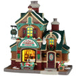 This image shows what this Lemax building looks like on a white background. It was designed to look like a tall cottage turned into a store. The roofs and the sidewalks are covered in snow. There are Christmas decorations on the building and near the front door.