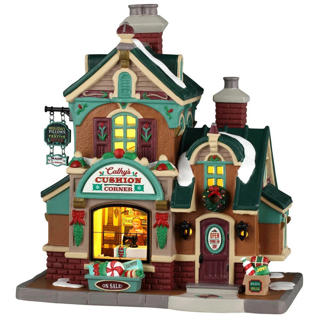 This image shows what this Lemax building looks like on a white background. It was designed to look like a tall cottage turned into a store. The roofs and the sidewalks are covered in snow. There are Christmas decorations on the building and near the front door.