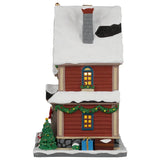 This image shows what this building looks like from the side. There's snow on the roofs and on the sidewalk. There are two windows. There's a decorated Christmas tree, as well as a garland.