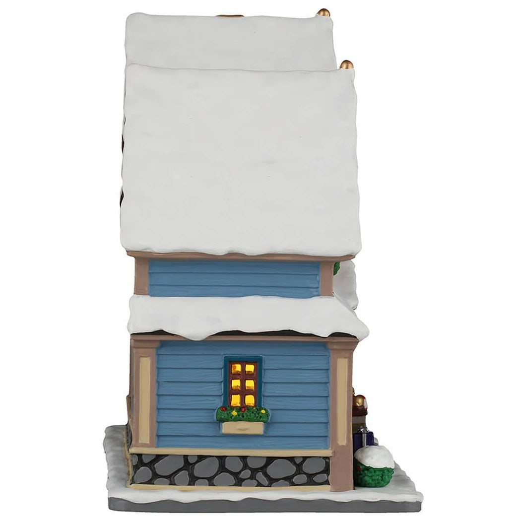 This image shows what the other side of this building looks like. The roof and the sidewalk are both covered in snow. There's a window with a planter attached and there are flowers in the planter.