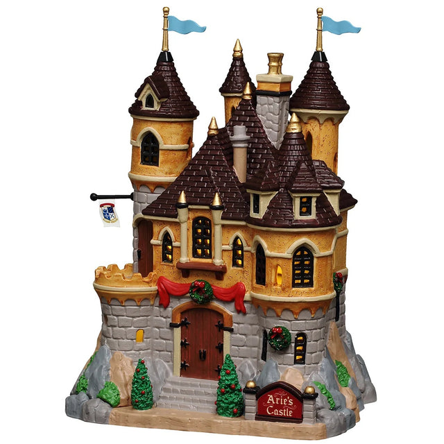 This image shows what this Lemax building looks like on a white background. It was designed to look like a large castle. There are blue flags on the steeples and decorated trees and wreaths. There's a sign near the front gate that reads "Arie's Castle."